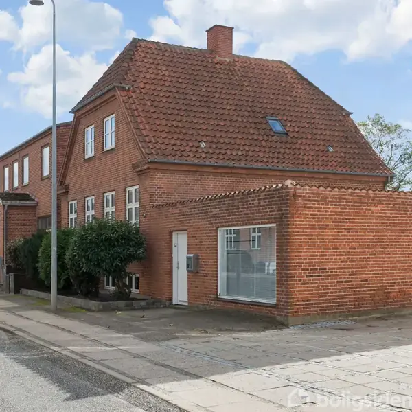 Et rødt murstenshus med skråt tag står stille langs en vej i en by; omgivet af fortov, gadelamper og lignende bygningsstruktur.