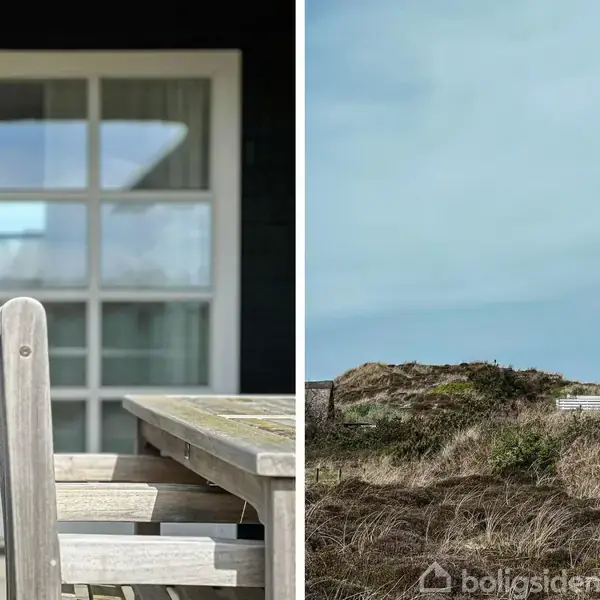 Et udendørs træbord står foran en stor glasdør, og i den anden del af billedet ses et hus med stråtag bag klitter. Atmosfæren er rolig og naturlig.