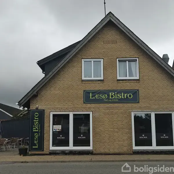 En bygning med skiltet "Læsø Bistro – Mad og café" på facaden. Udenfor står et par caféborde og stole. Bygningen er omgivet af en grå himmel og nabohuse.