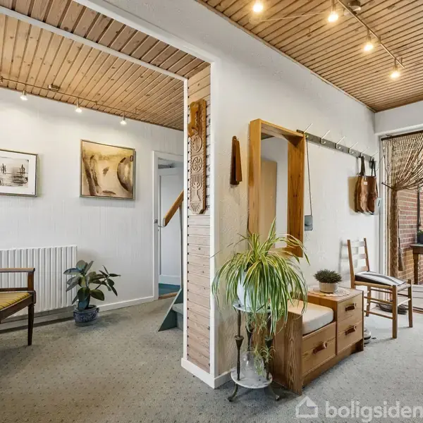 Entréhall med træbeklædt loft; dekoreret med kunst på væggene, planter og møbler; fører til en balkon med udsigt til en have.