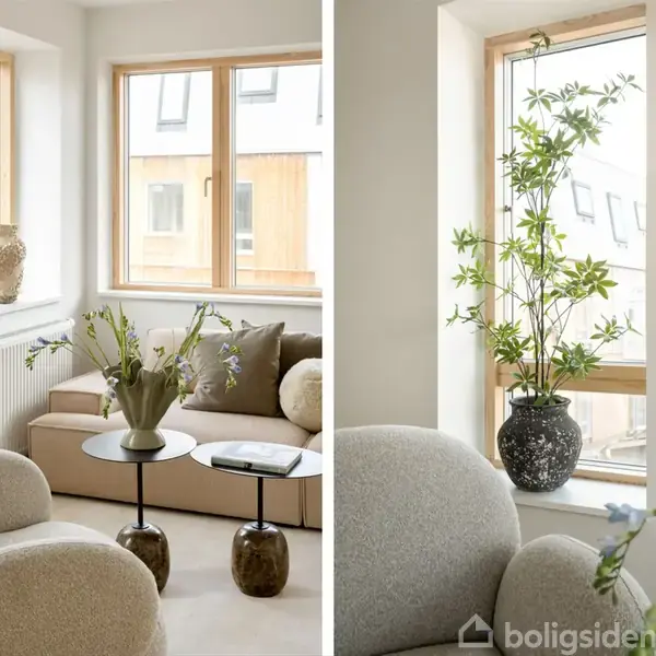Stue med beige sofa og stole, blomster i vase på sofabord, lys trærammevindue, moderne kunst på væggen, lyse vægge, naturligt lys strømmer ind, potteplante på vindueskarm.