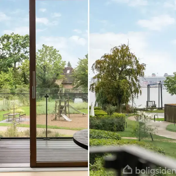 En åben altandør leder ud til en balkon med glasrækværk, hvorfra der ses en legeplads i en grøn have. Ved siden af er der en stiforbindelse mellem bygninger.