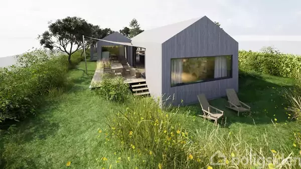 Et moderne, gråt hus med store vinduer står blandt frodigt grønt græs og vilde blomster. To liggestole er placeret foran huset, omgivet af buske og træer i baggrunden.