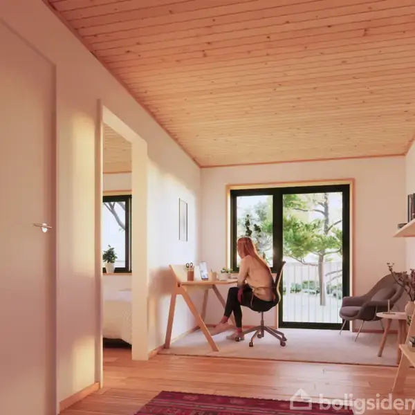 En person sidder ved et skrivebord i et lyst rum med trægulv og -loft. Store vinduer med udsigt til grønne træer skaber en lys og indbydende atmosfære.