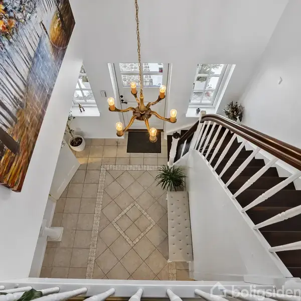 Et to-etagers hus står i et snedækket landskab. Huset har en altan, sort tag og hvide rammer. Foran huset står havemøbler på en terrasse.