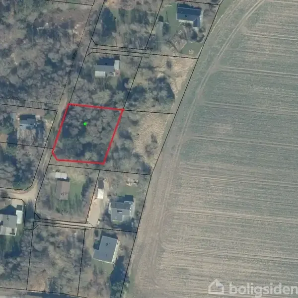 Luftfoto viser et område med huse og træer indrammet af en rød firkant. Til venstre ses flere bygninger og beboelsesområder. Til højre er der en stor mark uden bebyggelse.