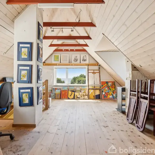 Loftværelse med malerier på vægge og gulv, arbejdsstol ved skrivebord, og stablede stole til højre. Træpaneler beklæder væggene, og et vindue giver udsigt til træer. Karton med "jem & fix".
