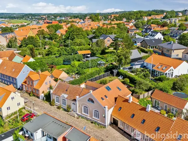 En hvid skoreol med kurve og vaser med grene står i en entré. En brun frakke hænger på et grønt stumtjener. Baggrunden har en hvid dør med buet rude.