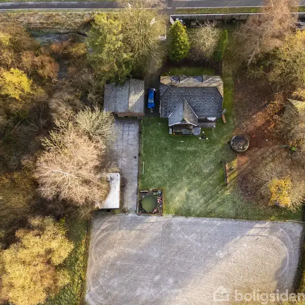 En enkeltstående bygning omgivet af træer set oppefra. Bygningen ligger i et grønt område med en grusplads foran. Den omgivende natur er fyldt med forskellige slags træer.