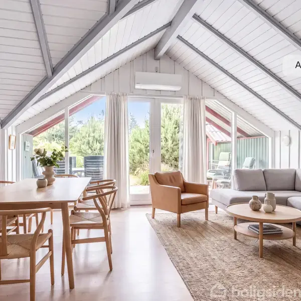 Et lyst, skandinavisk interiør viser en stue med en grå sofa og træbord ved siden af en stol. Store glasdøre åbner til en terrasse og præsenterer udsigt til træer. Tekst: "AI visualisering".