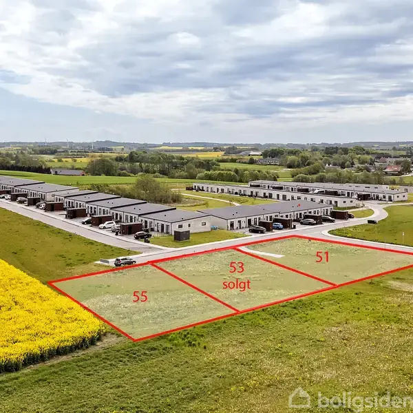 Tre byggegrunde markeret med numrene 51, 53 (solgt), og 55 ligger ved siden af et boligområde. En mark med gule blomster grænser op til grundene. Skyet himmel i baggrunden.
