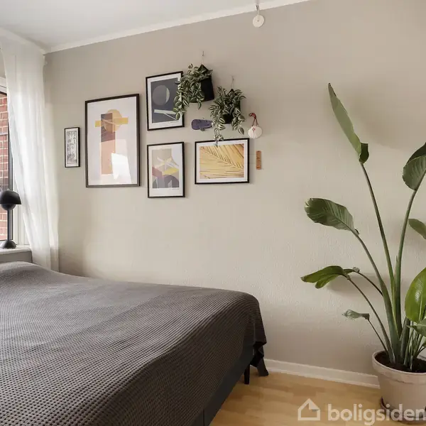 Soveværelse med stor seng og gråt sengetæppe. Væggen har billeder og planter. Ved siden af vinduet ses en stor grøn plante i en potte på trægulvet.