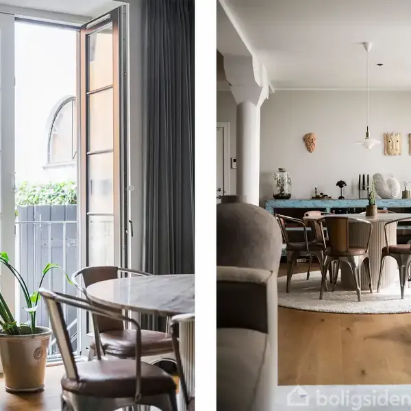 En åben dør leder til en balkon med grønne planter. Ved siden af er en spisestue med runde bord og stole, omgivet af kunst på væggen og en stor plante ved siden af vinduet.