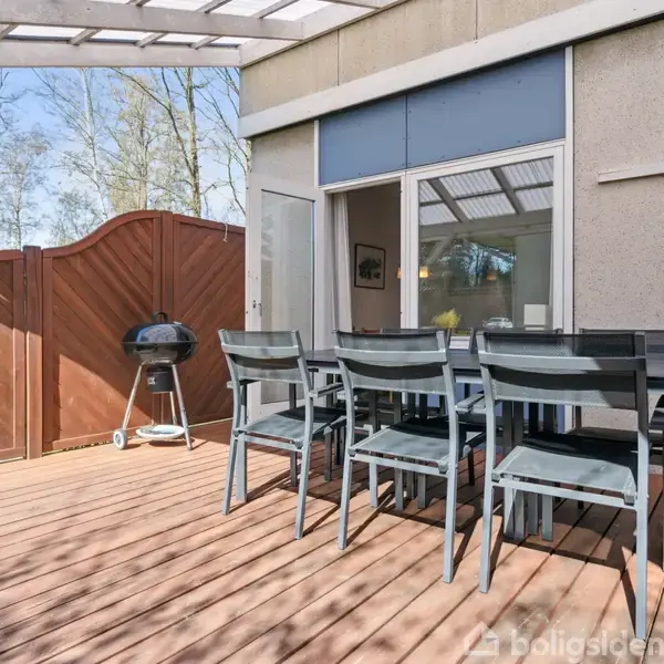 En stue med en fladskærms-tv på væggen over en kommode. En sofa og et bord står i forgrunden. En åbning fører til en entré med garderobe.