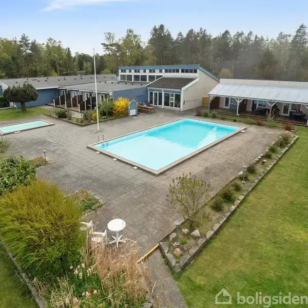 Et køkken med lyse træskabe, en vask og en opvaskemaskine til højre. En dør bagerst har en måtte foran, og vægge er dekoreret med viskestykker.