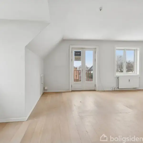 Stue med lyse trægulve uden møbler; døre åbner til balkon, vinduer lader dagslys ind. Væggene er hvide, og der er udsigt til omkringliggende træer. Skilt på døren: "3031".