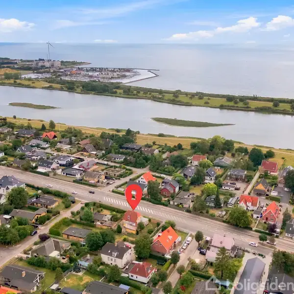 Boliger langs en vej med rødt tag markeres af en rød nål. Baggrunden viser søer og åbent landskab under en blå himmel.