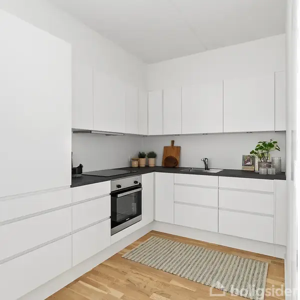 Hvidt køkken med sorte borde, ovn og kogezone. Skærebræt, planter og en vask på bordet. Tæppe på gulvet i et lyst rum.