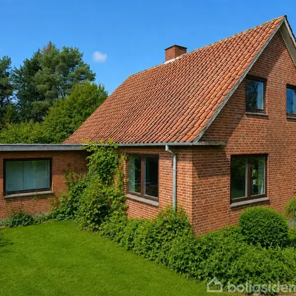 Et murstenshus med rødt tag står i en grøn have. Planter vokser op ad husets facade, omgivet af buske og træer. Himlen er blå med få skyer.