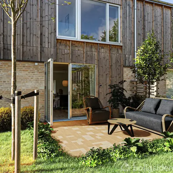 Et moderne rækkehus med træ- og murstensfacade har åbne glasdøre til en terrasse med sofa og bord. Omkring terrassen ses grønne planter og en velholdt græsplæne.