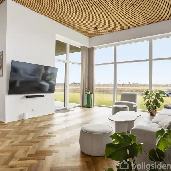 En rummelig garage med to hvide, lukkede porte, tom gulvplads og en væg med opbevaring. I baggrunden er der en dør til et tilstødende rum.