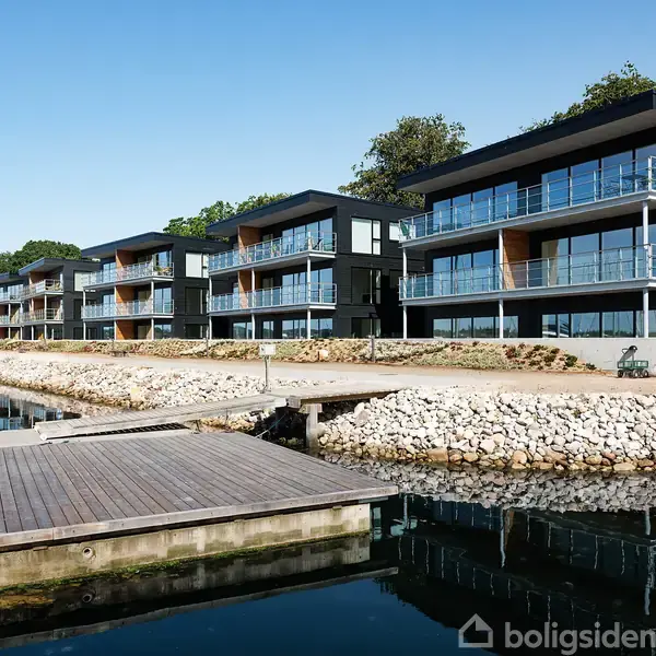 Store glasdøre åbner ud mod en marina fyldt med både, der ligger til kaj. Vandet er roligt, og der er skov og himmel i baggrunden.