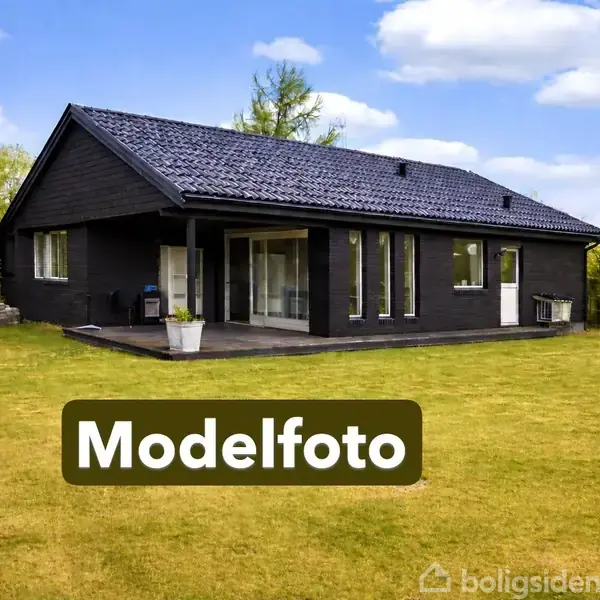 Sort, moderne hus med store vinduer står på en velplejet græsplæne omgivet af træer under en blå himmel. Tekst: "Modelfoto".