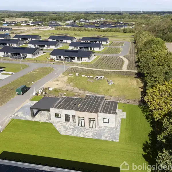 En enkeltstående moderne bygning med fladt tag og store vinduer står på en græsplæne. Omkringliggende boligkvarter fyldt med ens parcelhuse. Skovområde i baggrunden.