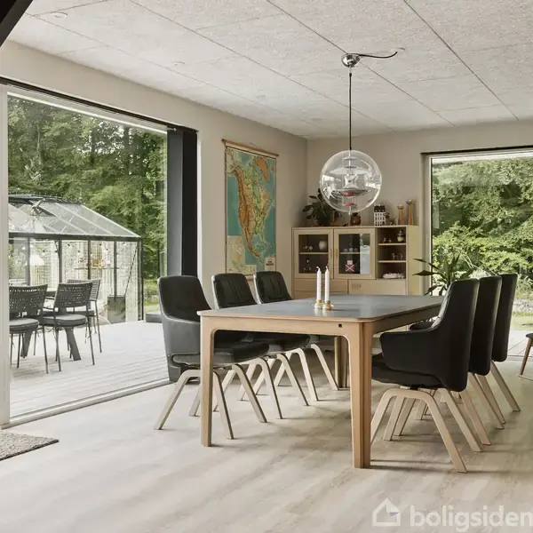 Spisebord med sorte stole står i en lys spisestue med åbne glasdøre ud til en terrasse. En globuslampe hænger over bordet; skov ses udenfor.