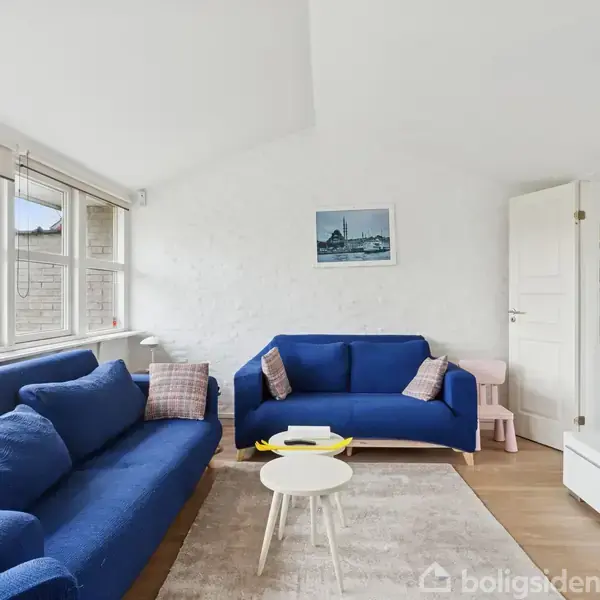 To blå sofaer står overfor hinanden i en stue med lyse vægge. Der er et lille sofabord imellem dem og et tv i højre side. Et billede hænger på bagvæggen.