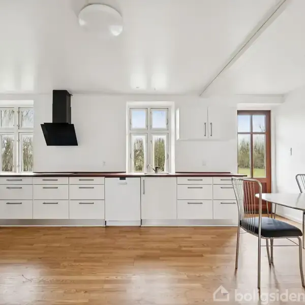 En stor, traditionel bygning står stille i et åbent, græsklædt område med klare himmel og få træer i baggrunden.