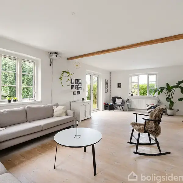 Sofa i rummelig stue med lyse trægulve og store vinduer. Flere planter og billeder på væggene. Lyst, moderne indretning med gyngestol og sofabord. Ingen tekst.