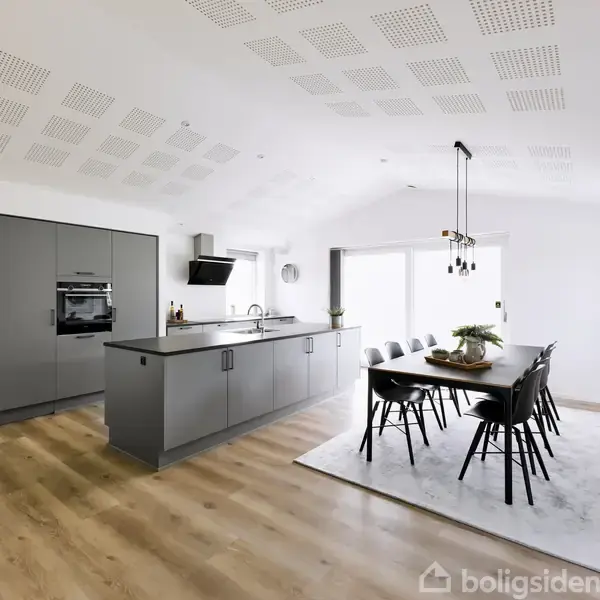 Køkken i moderne design omfatter gråt køkkenø med indbyggede apparater og sort spisebord med otte stole, i en lys, rummelig stue med trægulv og store vinduer.