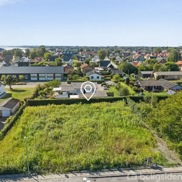 En åben grund med høj vegetation omgivet af huse i en forstadskvarter. En ikonisk markør placerer en hvid enetages bygning midt i området.