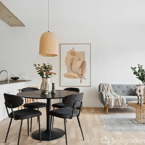 Rundt spisebord med fire sorte stole, dekoreret med blomster, i et moderne, lyst hjem. Til højre en grå sofa ved et sofabord og abstrakt kunst på væggen.