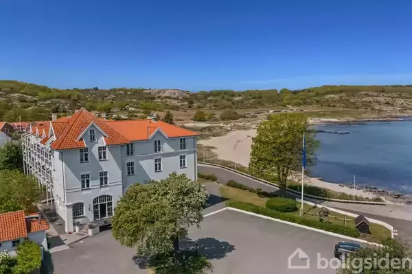 Et billardbord midt i et lyst rum, omgivet af stole og spejle. Ved siden af er der åbne franske døre, der fører til en stue med udsigt til havet.