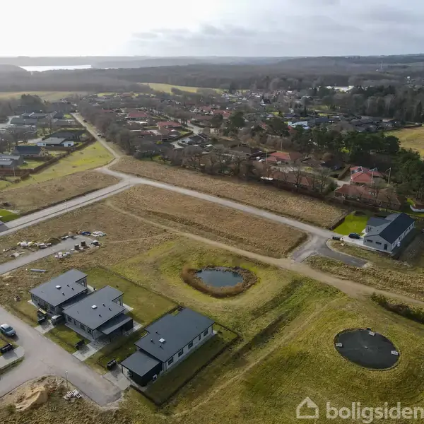 Boligområde set fra luften med moderne huse i forgrunden. Omkringliggende marker og bebyggelse strækker sig mod horisonten. Små søer og veje danner mønstre i landskabet.