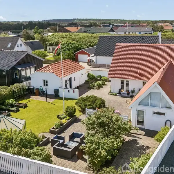 Hus med rødt tag står stille i et velholdt haveområde med græs, havepavillon og udendørsmøbler. Omkringliggende huse og grønne områder ses i baggrunden.