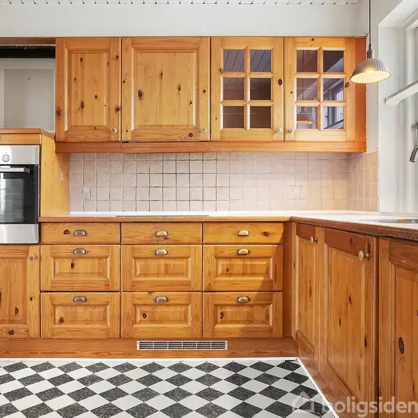 Et køkken med træskabe og integreret ovn står i et rum med ternet sort-hvidt gulv. Der er en lysarmatur over vasken ved siden af et stort vindue.