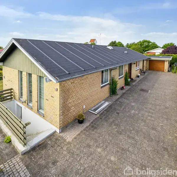 Huset er en én-etagers murstensbygning med sort tag. Det ligger på en stor grund med en lang indkørsel og grønne omgivelser i et roligt villakvarter.