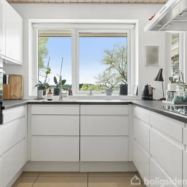 Et spisebord med stole står i midten af et rum. Det er dækket med en lys løber og har to stearinlys. Til højre ses en ôbning til et værelse med stol.