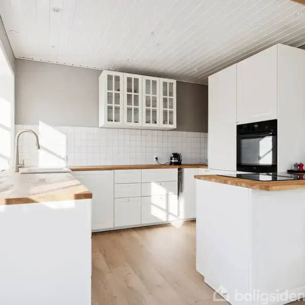 Køkken i moderne stil med hvide skabe og indbyggede apparater. Lys træbordplade omkranser rummet. I konteksten ses et skilt med teksten: "Livet er lavet for store og små øjeblikke."