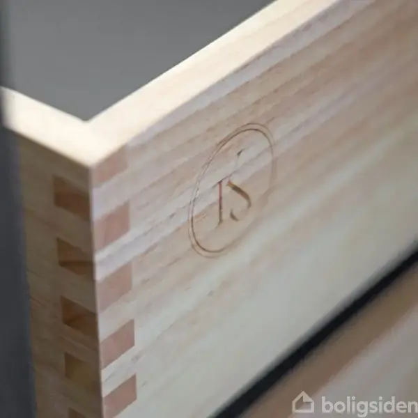 En hvid væg med et dobbelt stikkontakt. Sollys kaster en skygge diagonalt på væggen og gulvet. Minimalistisk og lys indendørs atmosfære.