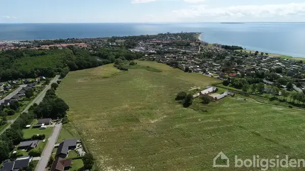 En stor grøn mark strækker sig mod havet i baggrunden, mens en by med huse omgiver marken til højre og venstre.