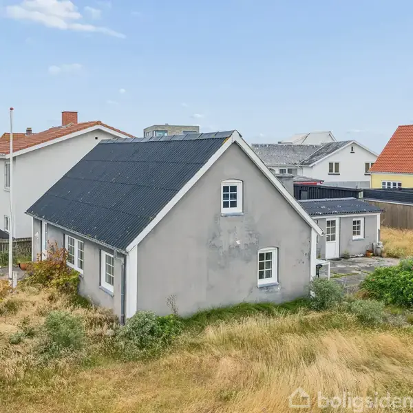 Grå hus med sort tag står stille i en række af huse. Omgivet af græs og en mindre have, er det sat i en fredelig nabolagsscene.