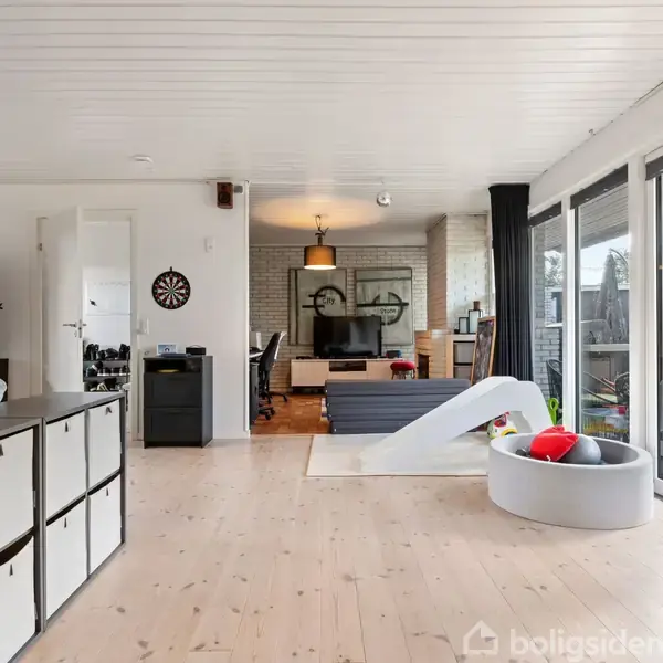Stue med tv og sofa, børnelegetøj og skydedøre til terrasse. Indrettet med lyse trægulve, en dartskive og kontorhjørne.