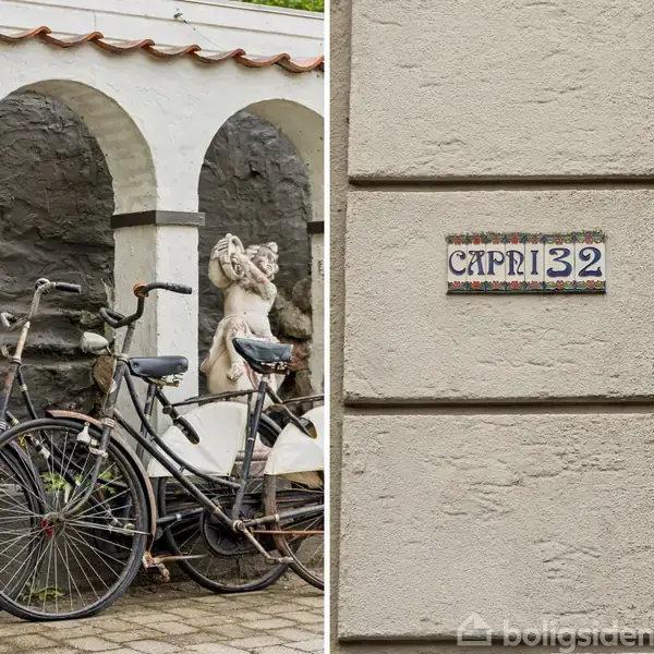 To cykler er parkeret foran en bygning med hvide buer og en statue. Ved siden af er der en væg med skiltet "CAPRI 32".