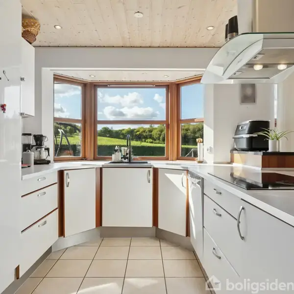 Et moderne køkken med hvide skabe og apparater. Store vinduer giver udsigt til en grøn have. Køkkenet er lyst og rummeligt med en central kogeplade og udsugningssystem.