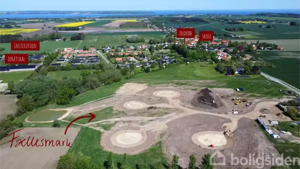 Dronebillede af et åbent landskab med jordarbejde og marker. En pil peger mod et område markeret som "Fællesmark". I baggrunden er der huse, institution, idrætshal, indkøb og skole.