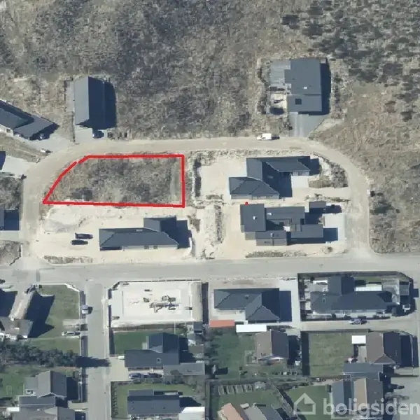 Grund markeret med rød linje i beboelsesområde. Omkringliggende er flere huse arrangeret langs stier og veje i en etableret bebyggelse. Området virker nyudviklet med forskellige tomme eller halvt byggede grunde.